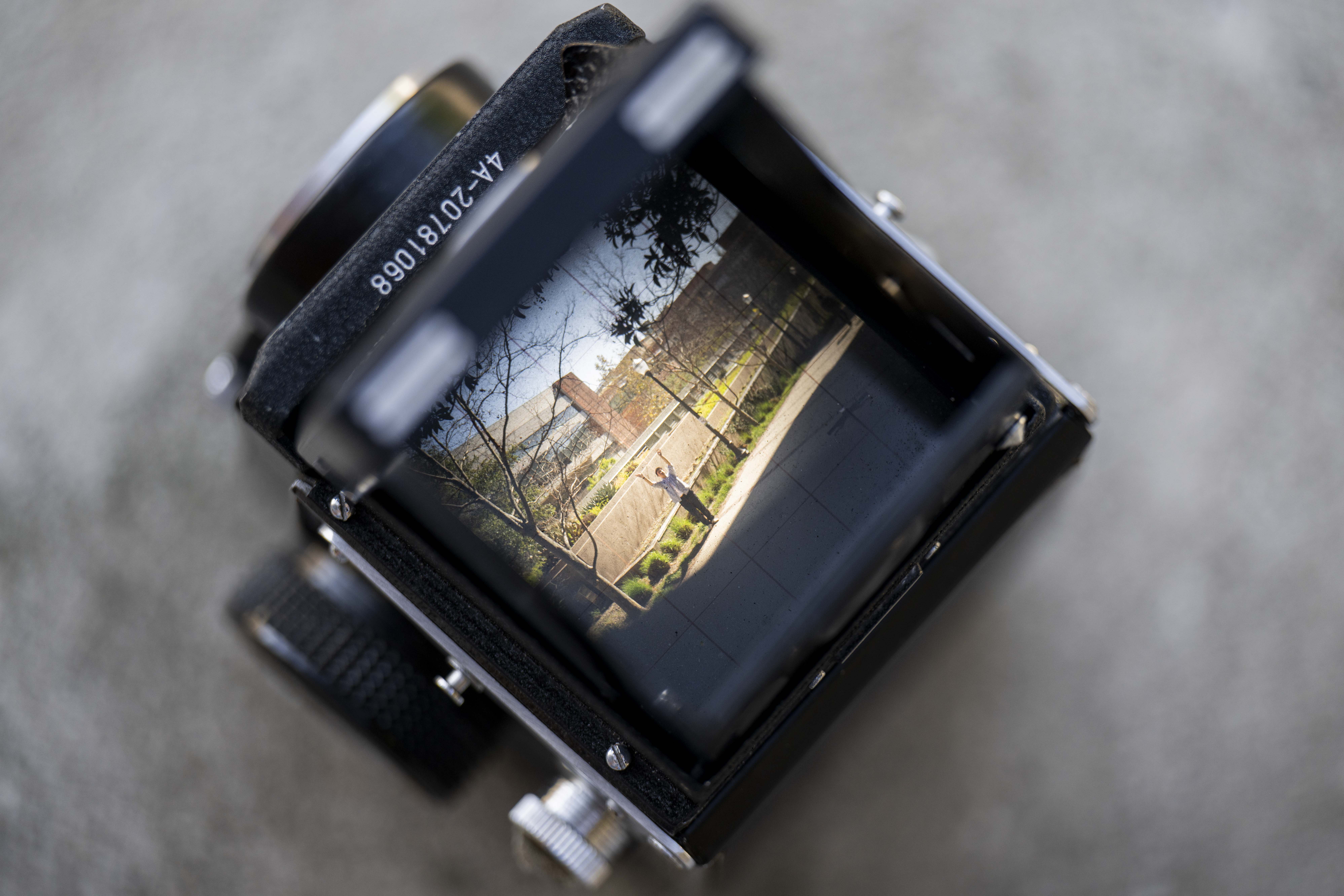 An image of a digital camera with a person standing on a sidewalk viewed through the lens.